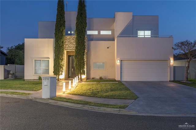 modern home featuring a garage, fence, a front lawn, concrete driveway, and stucco siding