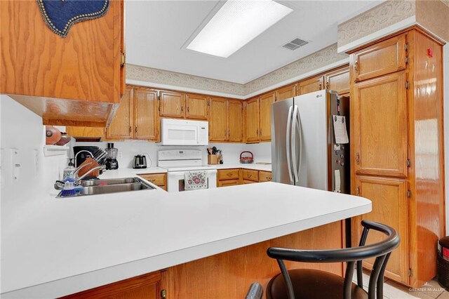 1700 Aries St, Mission, TX 78572 - kitchen with white appliances, a peninsula, light countertops, brown cabinets, and a breakfast bar