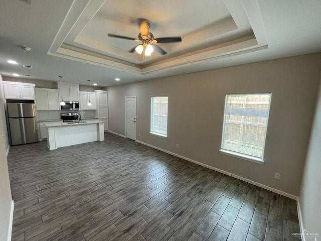 unfurnished living room featuring ceiling fan, dark hardwood / wood-style flooring, and a tray ceiling