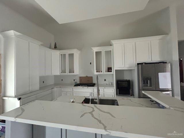 kitchen with sink, stainless steel refrigerator with ice dispenser, light stone counters, white cabinets, and a kitchen island