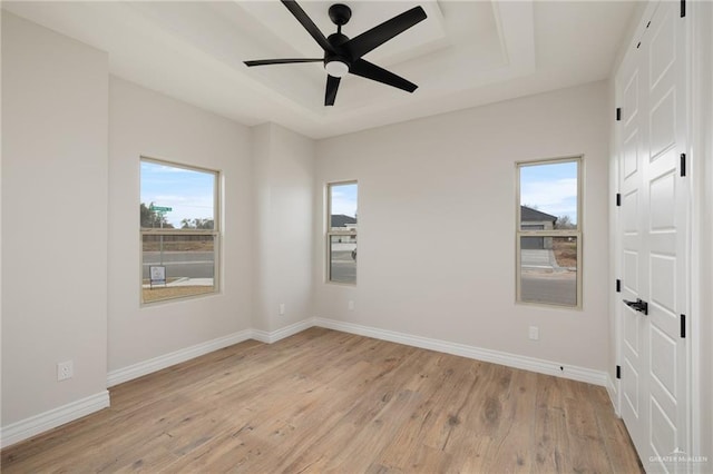 spare room with ceiling fan, a raised ceiling, and light wood-type flooring