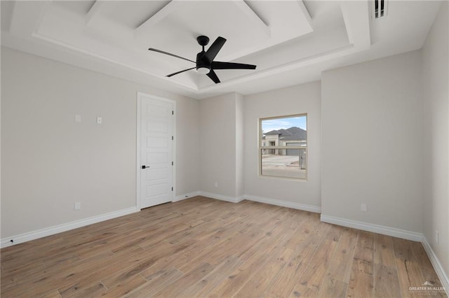 empty room with a tray ceiling, ceiling fan, and light wood-type flooring