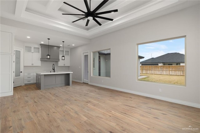 kitchen with sink, white cabinets, hanging light fixtures, a kitchen island with sink, and light hardwood / wood-style floors