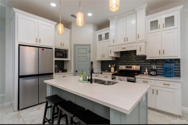 kitchen featuring white cabinetry, hanging light fixtures, stainless steel appliances, decorative backsplash, and a kitchen island with sink