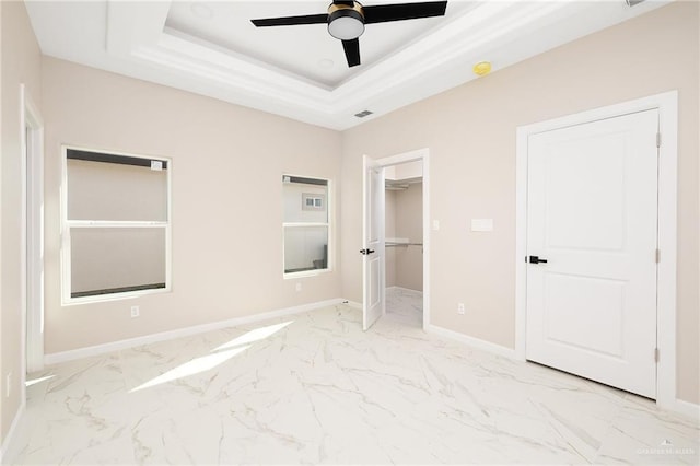 unfurnished bedroom featuring ceiling fan, a raised ceiling, a walk in closet, and a closet