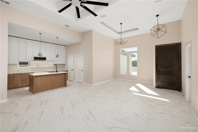 kitchen featuring pendant lighting, sink, white cabinetry, and an island with sink