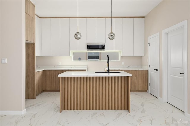 kitchen featuring sink, white cabinetry, an island with sink, and hanging light fixtures