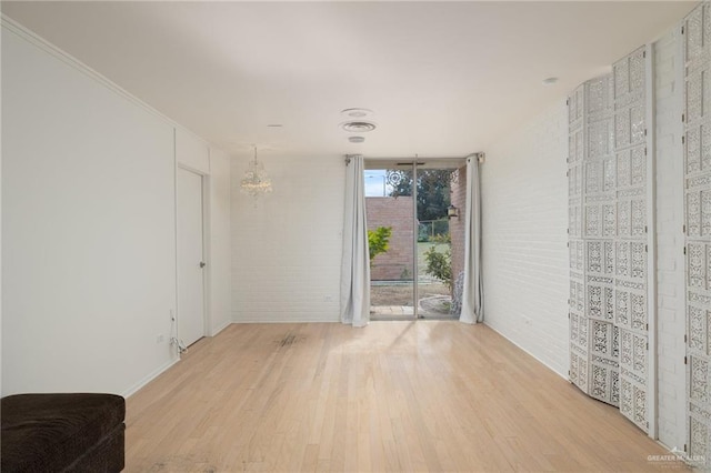 unfurnished room featuring expansive windows, brick wall, an inviting chandelier, and light hardwood / wood-style flooring