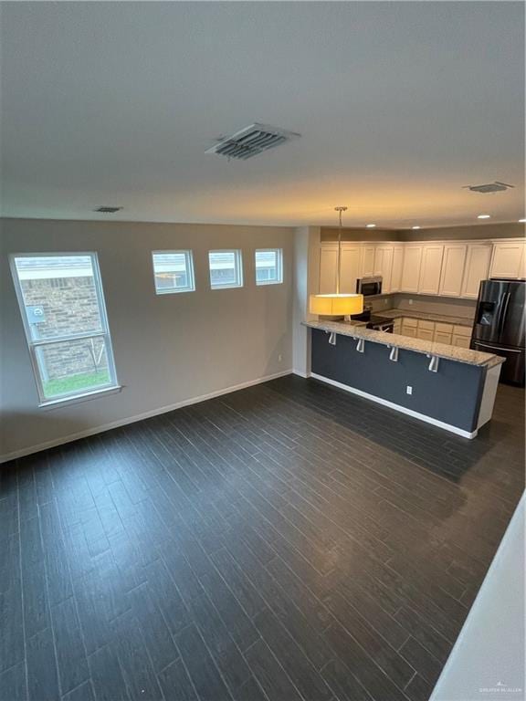 kitchen featuring white cabinetry, dark hardwood / wood-style floors, black fridge, decorative light fixtures, and kitchen peninsula