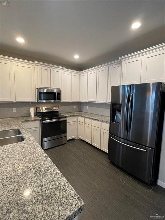 kitchen with appliances with stainless steel finishes, sink, white cabinets, light stone counters, and dark wood-type flooring