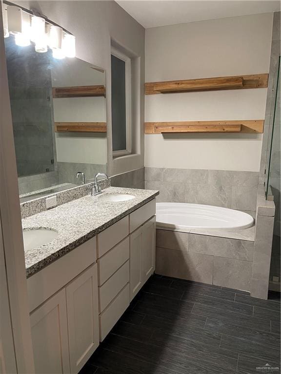 bathroom with hardwood / wood-style floors, vanity, and a relaxing tiled tub