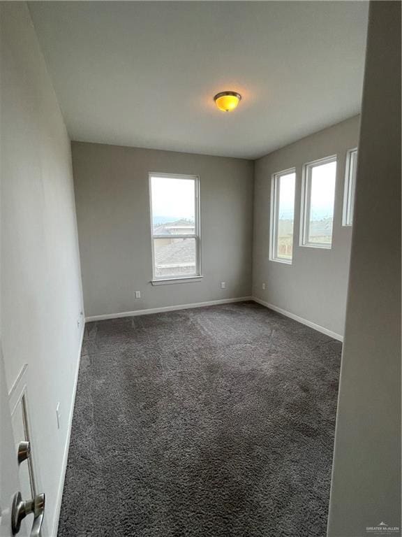 unfurnished room featuring dark colored carpet and a healthy amount of sunlight