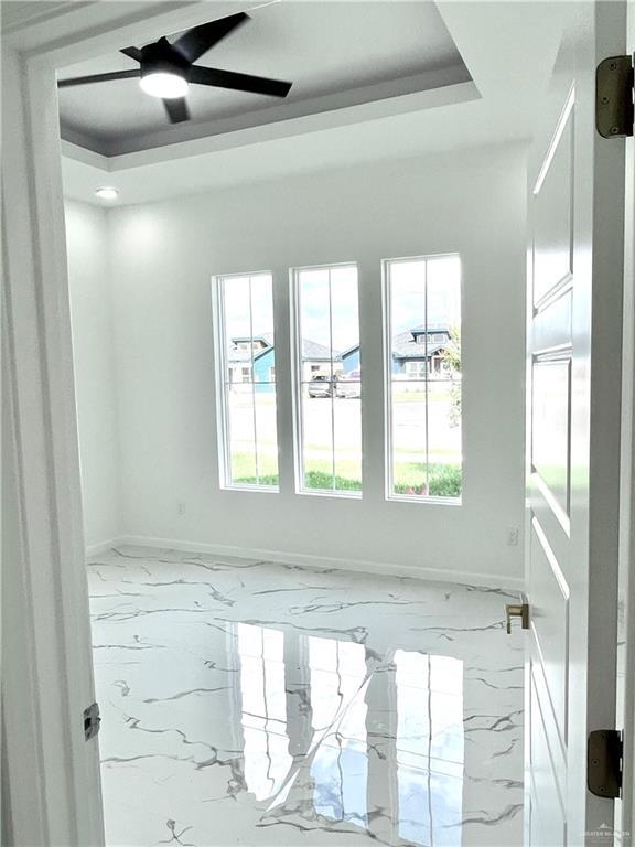 empty room with ceiling fan and a tray ceiling