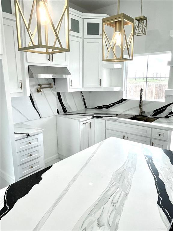 kitchen with sink, white cabinetry, hanging light fixtures, light stone countertops, and decorative backsplash