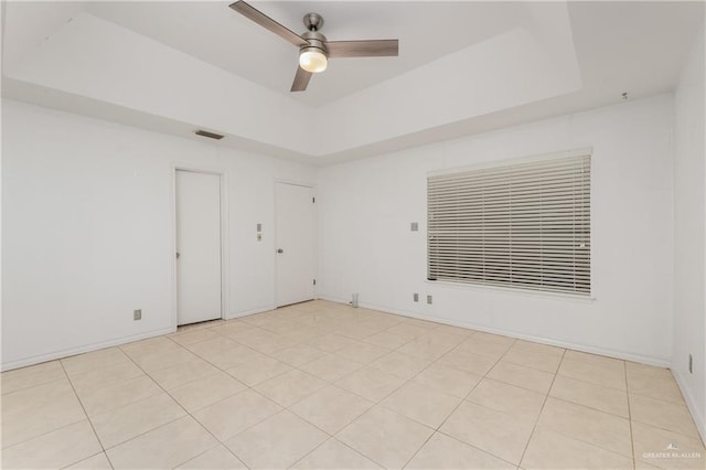 tiled spare room with ceiling fan and a tray ceiling
