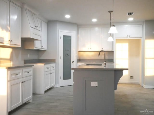 kitchen featuring white cabinetry, sink, hanging light fixtures, hardwood / wood-style floors, and an island with sink