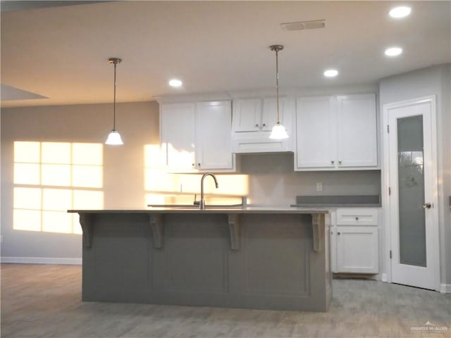 kitchen with white cabinetry, hanging light fixtures, and an island with sink