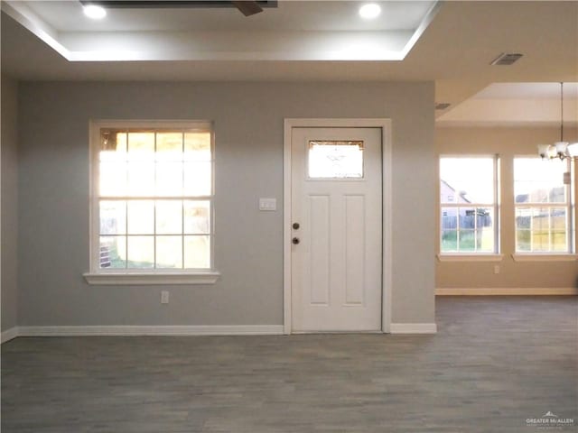 foyer entrance featuring a tray ceiling, dark hardwood / wood-style flooring, a healthy amount of sunlight, and a notable chandelier