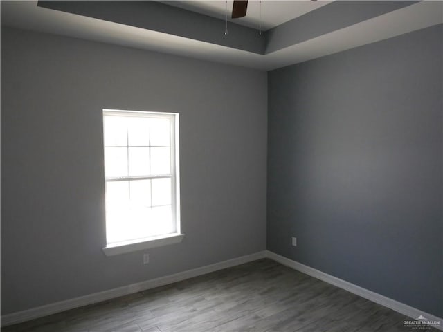 empty room with hardwood / wood-style floors, a tray ceiling, and ceiling fan