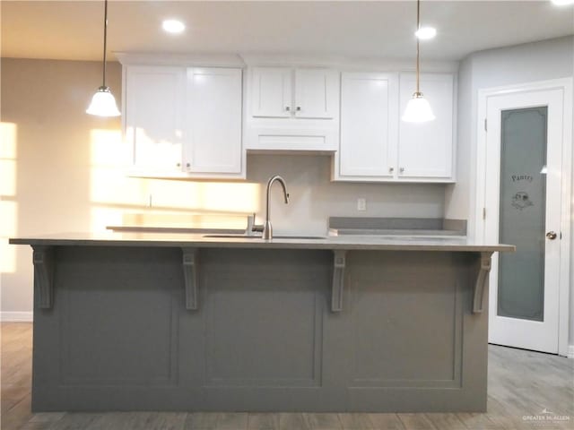 kitchen with a kitchen island with sink, white cabinetry, sink, and hanging light fixtures