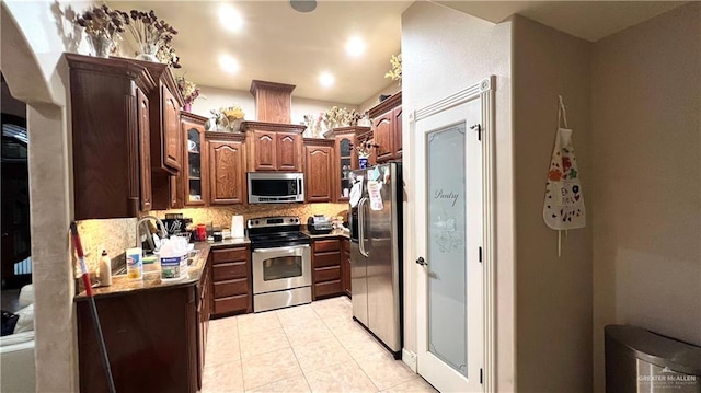 kitchen featuring backsplash, light stone countertops, light tile patterned floors, and appliances with stainless steel finishes