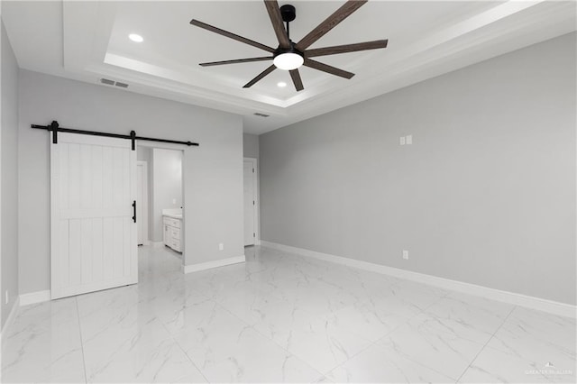 unfurnished bedroom featuring a barn door, a tray ceiling, ceiling fan, and ensuite bathroom