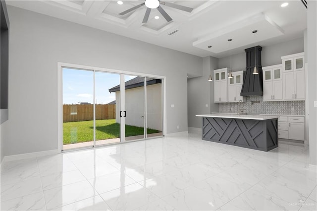 kitchen featuring tasteful backsplash, coffered ceiling, custom range hood, white cabinetry, and hanging light fixtures