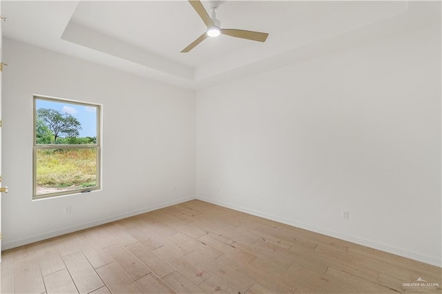 unfurnished room featuring a raised ceiling, ceiling fan, and light wood-type flooring