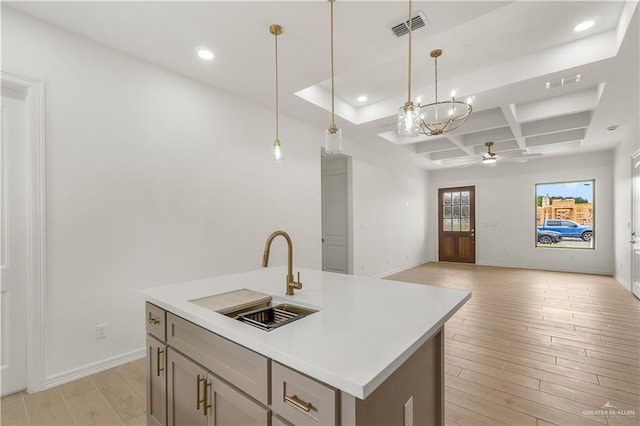 kitchen featuring coffered ceiling, sink, decorative light fixtures, light hardwood / wood-style flooring, and an island with sink