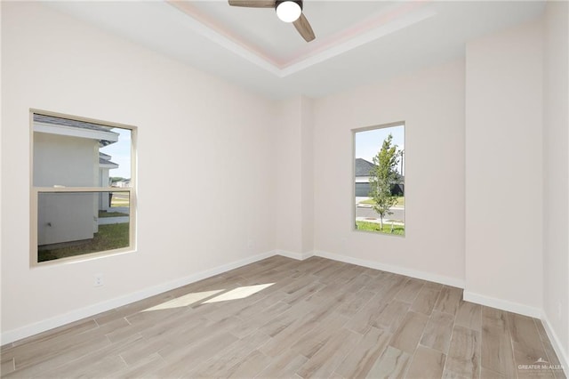 empty room featuring a tray ceiling, ceiling fan, and light hardwood / wood-style floors