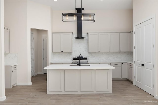 kitchen with sink, wall chimney range hood, a notable chandelier, a high ceiling, and hanging light fixtures