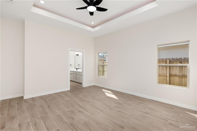 empty room with a tray ceiling, ceiling fan, and light hardwood / wood-style floors