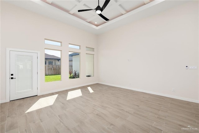 unfurnished room with coffered ceiling, ceiling fan, light hardwood / wood-style flooring, beamed ceiling, and a high ceiling