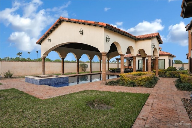 exterior space with a lawn, a tile roof, stucco siding, and an in ground hot tub