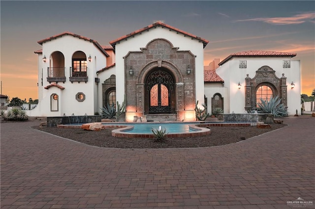 mediterranean / spanish-style house with a tile roof, stone siding, stucco siding, a balcony, and decorative driveway