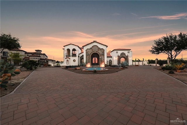 mediterranean / spanish-style home featuring stucco siding, stone siding, and curved driveway