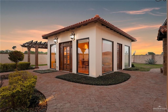 back of house at dusk with fence, a tile roof, stucco siding, a pergola, and a patio area