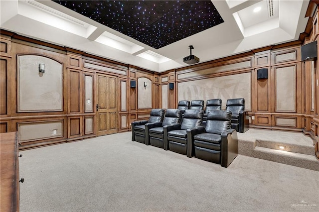 cinema room featuring a decorative wall, coffered ceiling, light colored carpet, and crown molding