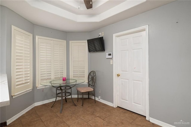 tiled dining space with ceiling fan and a tray ceiling