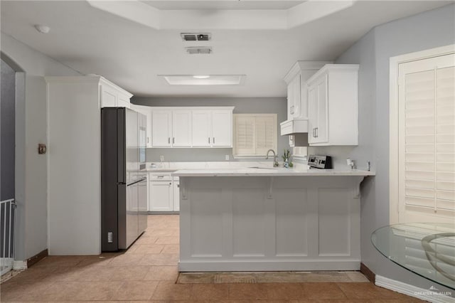 kitchen featuring sink, stainless steel refrigerator, a breakfast bar, white cabinetry, and kitchen peninsula