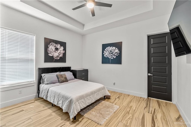 bedroom with a tray ceiling, baseboards, a ceiling fan, and light wood-style flooring