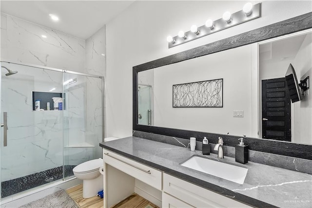 bathroom with toilet, wood finished floors, a marble finish shower, and vanity