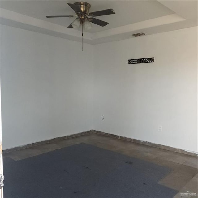 empty room with concrete flooring, ceiling fan, and a raised ceiling