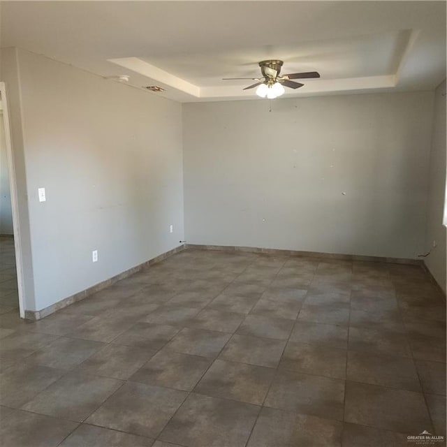 unfurnished room with ceiling fan and a tray ceiling