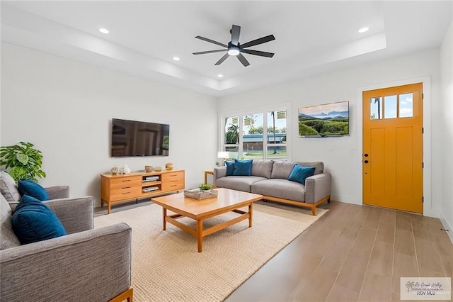 living area featuring a ceiling fan, baseboards, a tray ceiling, recessed lighting, and light wood-style floors