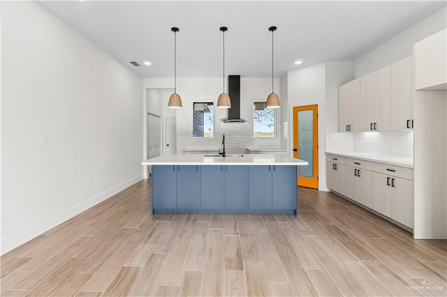 kitchen with a sink, wall chimney range hood, light countertops, baseboards, and wood tiled floor