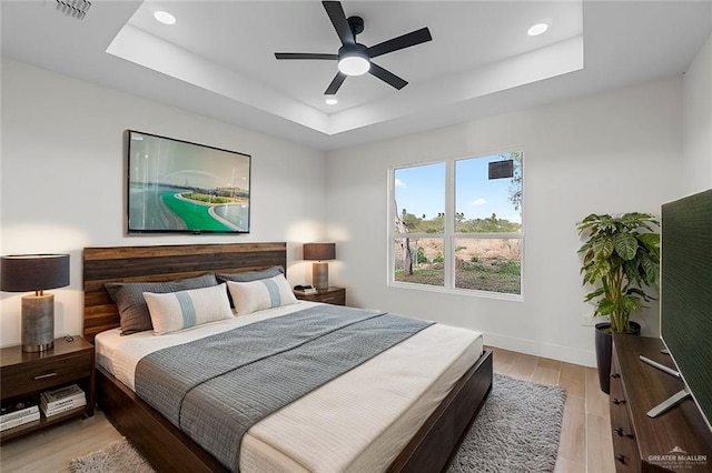 bedroom featuring baseboards, visible vents, a tray ceiling, recessed lighting, and light wood-style floors