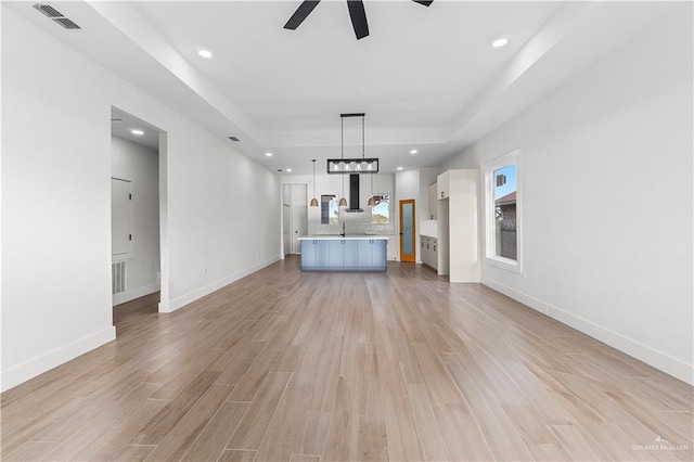 unfurnished living room featuring visible vents, recessed lighting, a raised ceiling, and light wood-style floors