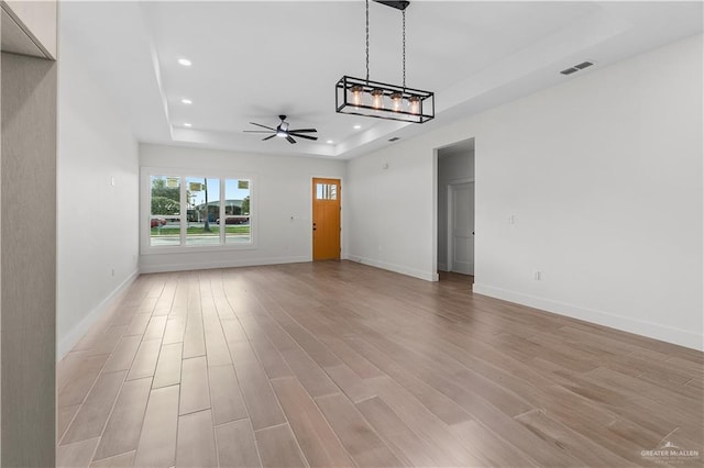 interior space with a tray ceiling, recessed lighting, visible vents, and light wood-type flooring