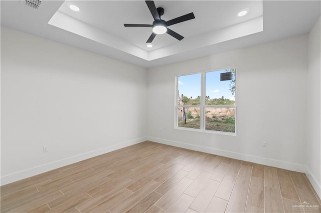 unfurnished room featuring a raised ceiling, a ceiling fan, baseboards, and light wood finished floors